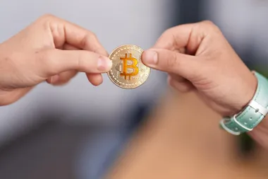 Dwie dłonie trzymają monetę bitcoin.