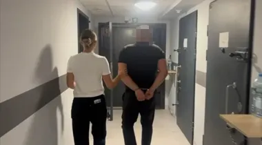 Funkcjonariuszka prowadzi zakuwanego w kajdankach mężczyznę korytarzem z celami w zakładzie karnym lub areszcie.