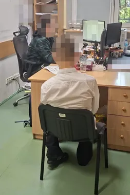 Dwie osoby siedzą przy biurku w pomieszczeniu biurowym, jedna z nich pracuje przy komputerze.