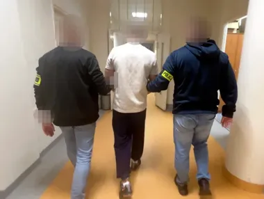 Funkcjonariusze policji prowadzą mężczyznę korytarzem budynku.