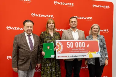 Cztery osoby pozują przed czerwoną ścianką z logo Mazowsze, trzymając duży czek na 50 000 zł dla Gminy Mała Wieś na zakup wyposażenia dla jednostek OSP oraz zie